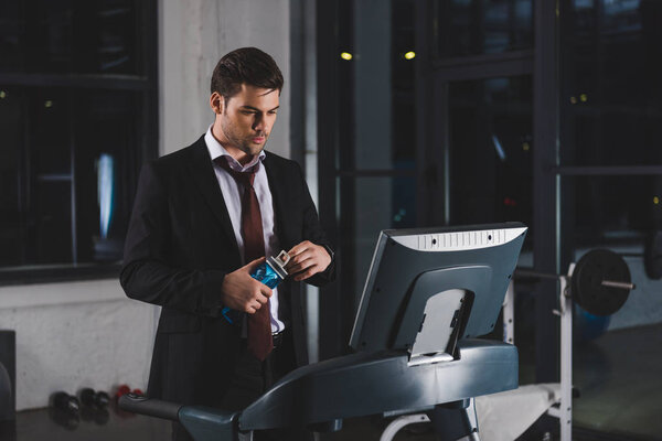 businessman in suit training on treadmill with bottle of water in sports center 