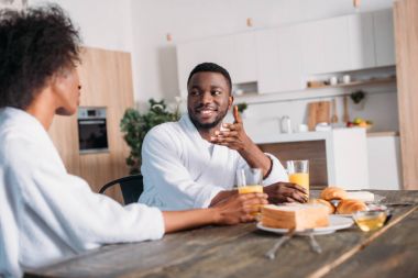 Kız arkadaşına kahvaltı masasında otururken konuşan Afrikalı-Amerikalı adam gülümseyen