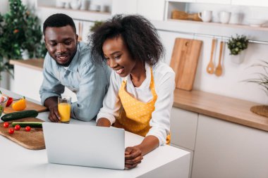 Genç çift eğleniyor dizüstü bilgisayar ile mutfakta gülümseyen