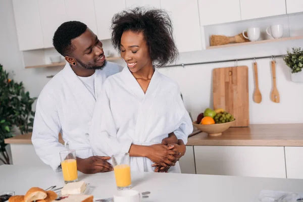 年轻男子拥抱微笑的女朋友 而站在餐桌上 早餐在厨房 — 免费的图库照片