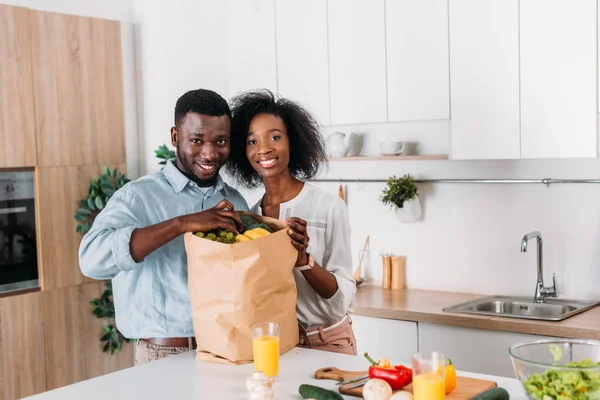微笑的非洲裔美国人夫妇从纸袋中取出葡萄和水果 — 图库照片
