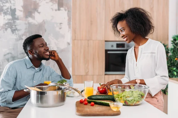 African american couple at table with vegetables, salad and pasta in saucepan