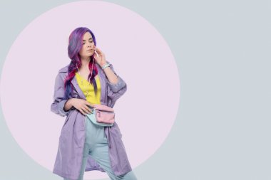 Mor trençkot yaratıcı arka plan üzerinde kulaklık ile müzik dinleme güzel genç kadın