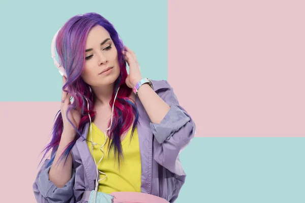 美丽的年轻妇女与五颜六色的头发在紫色的风衣听音乐与耳机 — 图库照片
