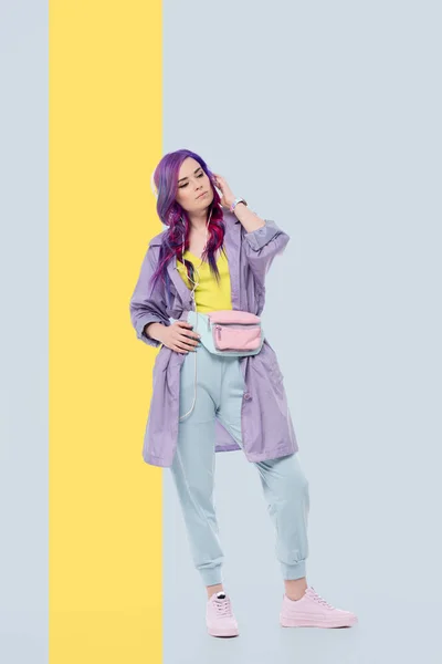 时尚的年轻女子穿着紫色的风衣听音乐与耳机的创作背景 — 图库照片