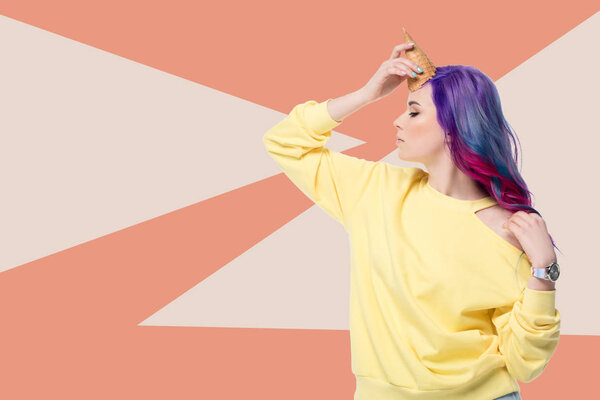 стильная молодая женщина притворяется единорогом с вафельным конусом на лбу на творческом фоне
