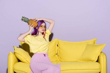 beautiful young woman sitting on yellow couch and holding pineapple near head clipart