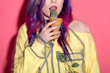 cropped shot of young woman in transparent coat licking cactus in waffle cone clipart