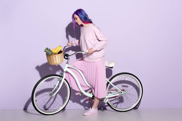 attractive young woman in pink clothing on bicycle with pineapple and bananas in basket