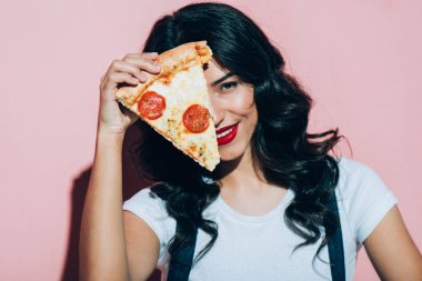 obscured view of beautiful smiling woman covering eye with piece of pizza on pink background clipart
