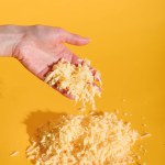 Plano recortado de mano femenina con queso rallado sobre fondo amarillo