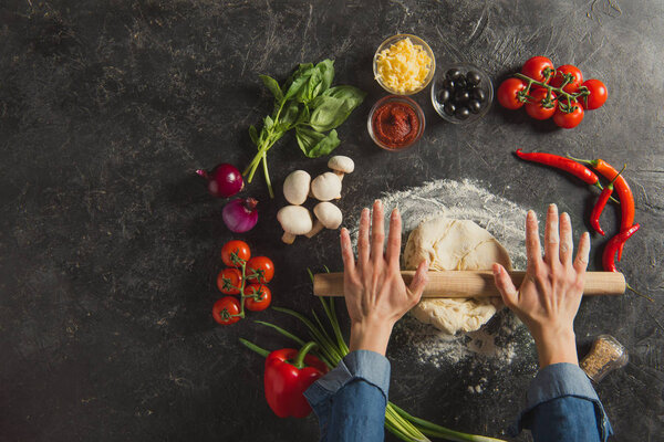 cropped shot of woman braking dough while cooking italian pizza on dark tabletop