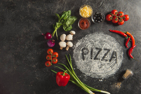 flat lay with fresh ingredients and pizza lettering made of flour on dark surface