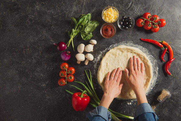 cropped shot of woman cooking italian pizza with fresh ingredients on dark tabletop