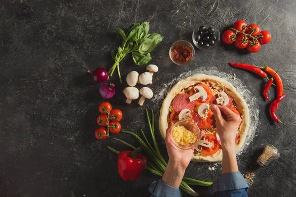 暗い卓上にイタリアのピザを料理しながら生地に粉チーズを入れて女性のショットをトリミング — ストック写真