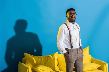 Elleri ceplerinde duran ve kameraya gülümseyen şık genç Afro-Amerikan adam 