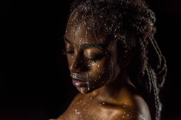 close-up view of seductive african american girl with milk drops on face and body isolated on black 