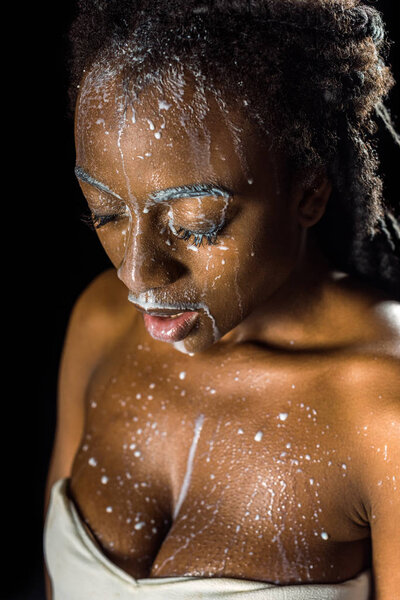 beautiful young african american woman with spilled milk on face isolated on black