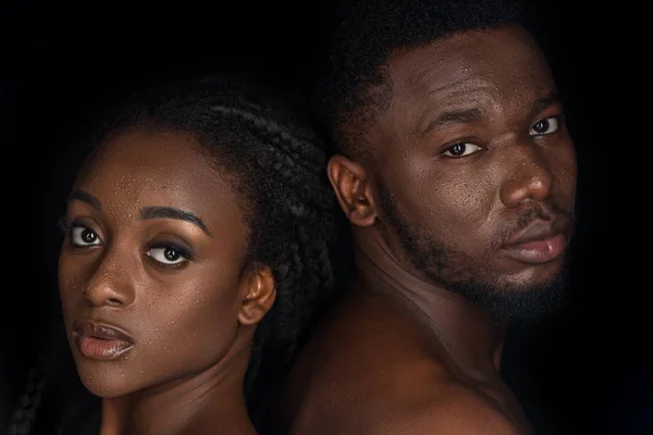 young african american couple with water drops on faces looking at camera isolated on black