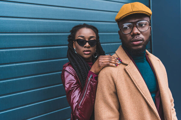 stylish young african american couple in jacket and overcoat posing together outside 