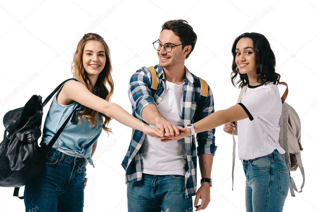 happy multicultural students putting hands together isolated on white