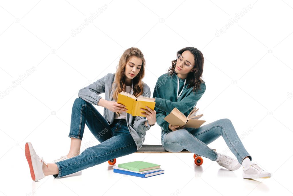 multicultural students sitting on skate with books isolated on white