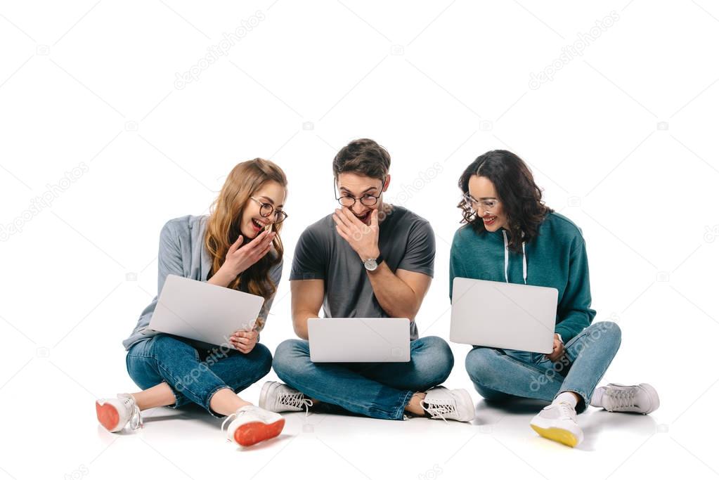 multicultural students laughing and using laptops on white
