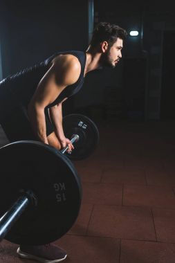Spor salonunda halter tutan genç vücut geliştirmeci yan görünüm