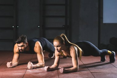 Young sportswoman and sportsman doing push ups in sports hall