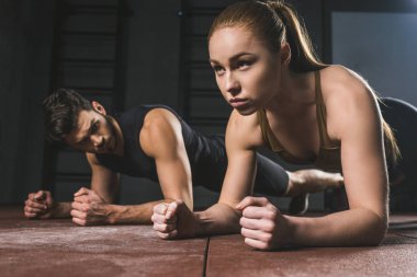 Young sportswoman and sportsman doing plank in gym clipart