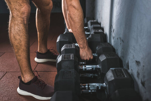 Cropped image of young sportsman raising dumbbell in sports hall