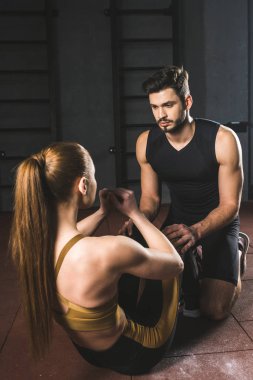 Male trainer helping young sportswoman to do abs in gym
