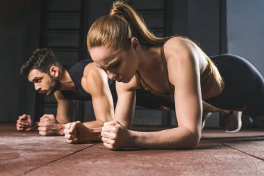 Young sportswoman and sportsman doing plank in gym