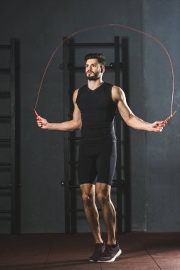 Genç sporcu spor salonunda ip atlama egzersizi yapıyor.