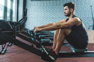 Young sportsman doing exercise on rowing machine in sports center