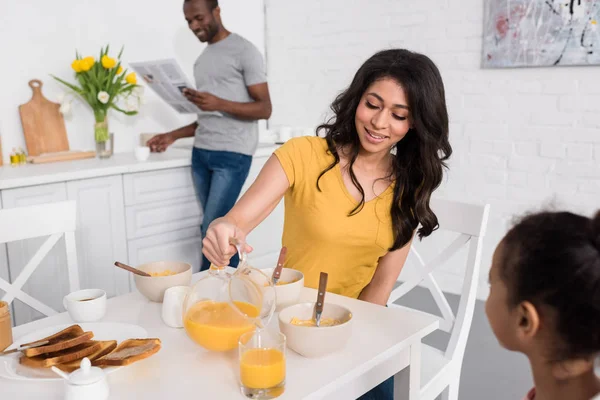 Happy Mother Pouring Orange Juice Daughter Breakfast While Father Reading — Stock Photo, Image