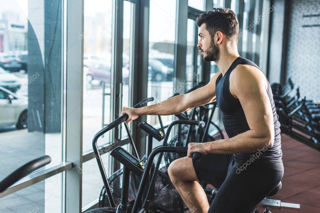 Side view of young sportsman doing workout on exercise bike in sports center