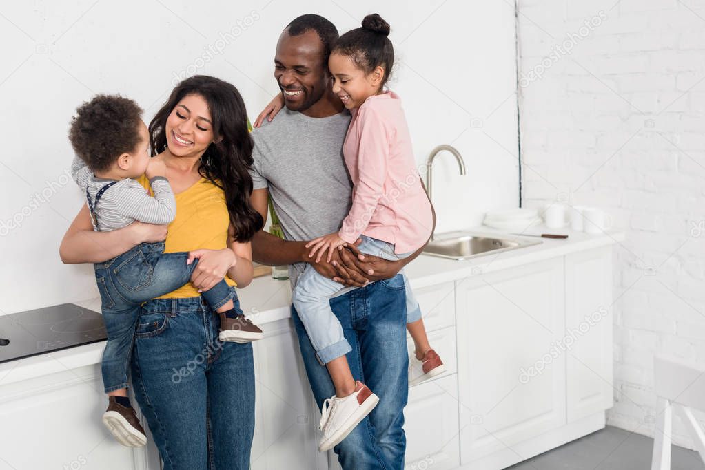 Happy young parents holding kids at kitchen
