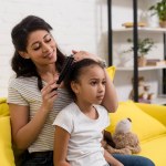 Junge glückliche Mutter kämmt Töchtern die Haare auf der Couch zu Hause