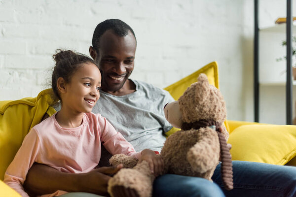 happy father and daughter playing with teddy bear together