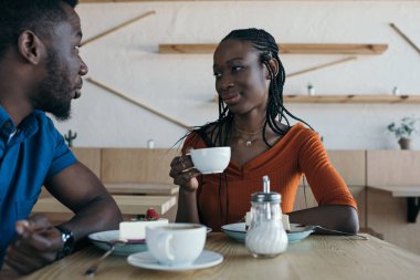 Afrika kökenli Amerikalı çift bardak kahve ve tatlılar kafede masada oturan