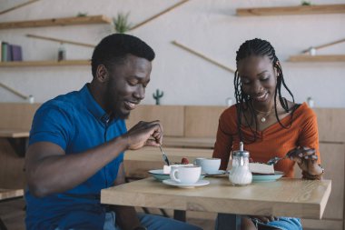 ile cups masadaki Afro-Amerikan çift kahve ve tatlılar kafede gülümseyen