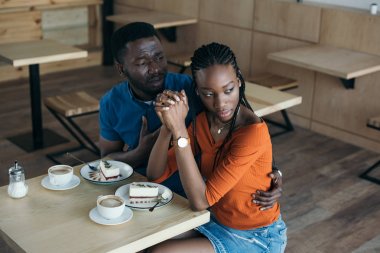 insulted african american woman with boyfriend sitting at table in cafe clipart
