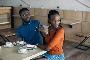 portrait of insulted african american woman with boyfriend sitting at table in cafe clipart