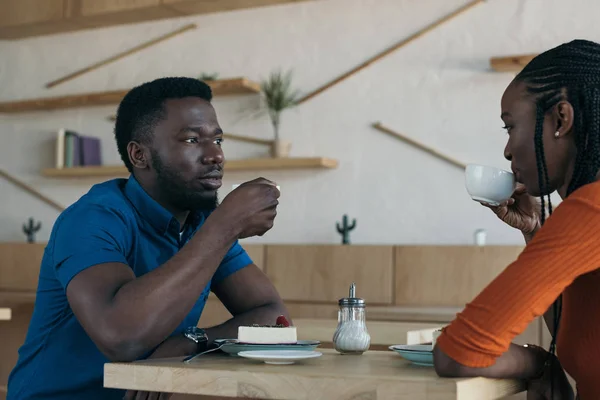 side view of african american couple drinking coffee at table in coffee shop