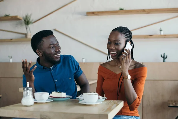 微笑的非洲裔美国妇女的肖像与男友在咖啡馆附近谈论智能手机 — 图库照片