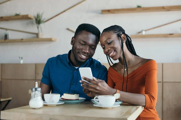 陽気なアフリカ系アメリカ人カップルのコーヒー ショップで一緒にスマート フォンを使用して — ストック写真