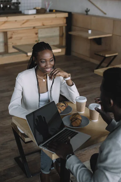 コーヒー ショップでノート パソコンをテーブルに座っているアフリカ系アメリカ人の友達に笑顔 — ストック写真