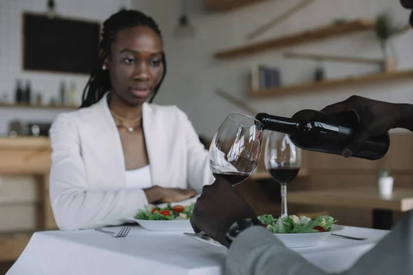 partial view of african american pouring wine into glass during romantic date with girlfriend in restaurant