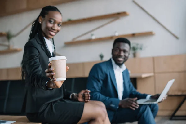 有选择的焦点微笑的非洲裔美国商人与笔记本电脑和同事显示咖啡去附近的咖啡馆 — 图库照片
